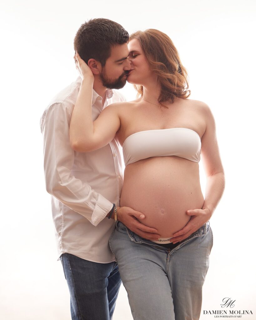 Portrait de grossesse : Complicité et amour à Strasbourg - Damien Molina - Photographe Photo lumineuse d'un couple attendant un enfant, la future maman tenant son ventre et le futur papa l'enlaçant tendrement, capturée à Strasbourg.