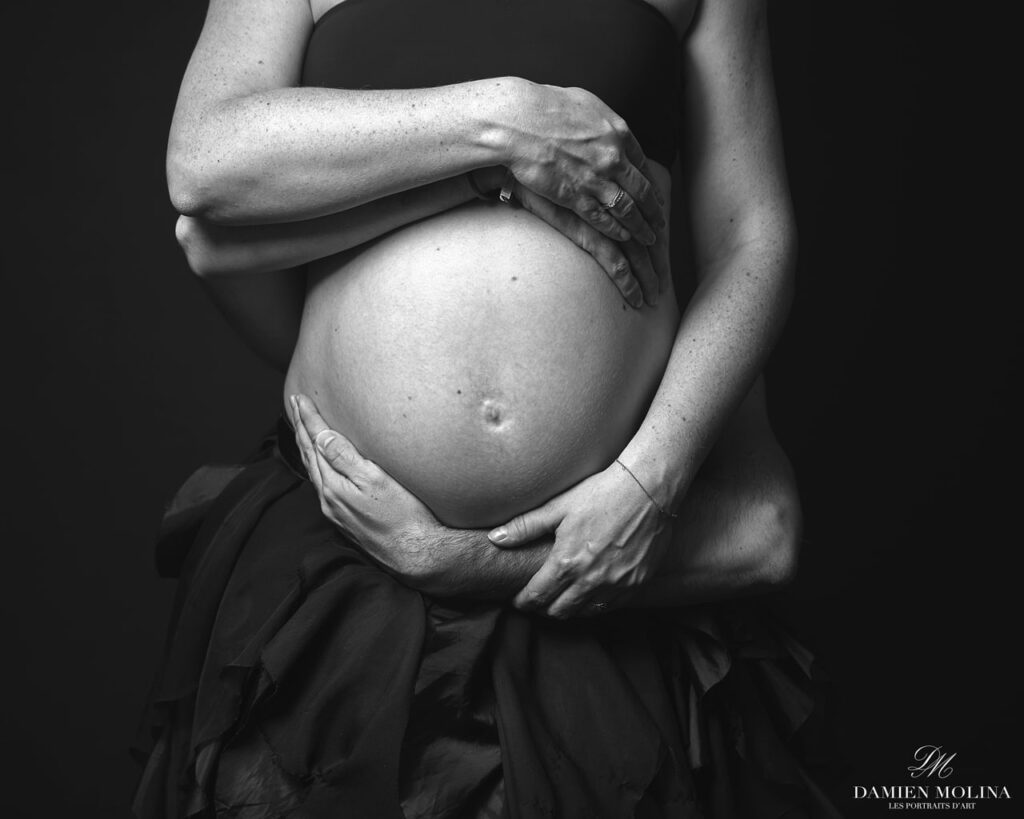 Portrait de grossesse : Émotion en noir et blanc à Strasbourg - Damien Molina - Photographe Photo en noir et blanc d'un couple posant leurs mains sur le ventre arrondi de la future maman, capturée lors d'une séance grossesse à Strasbourg.