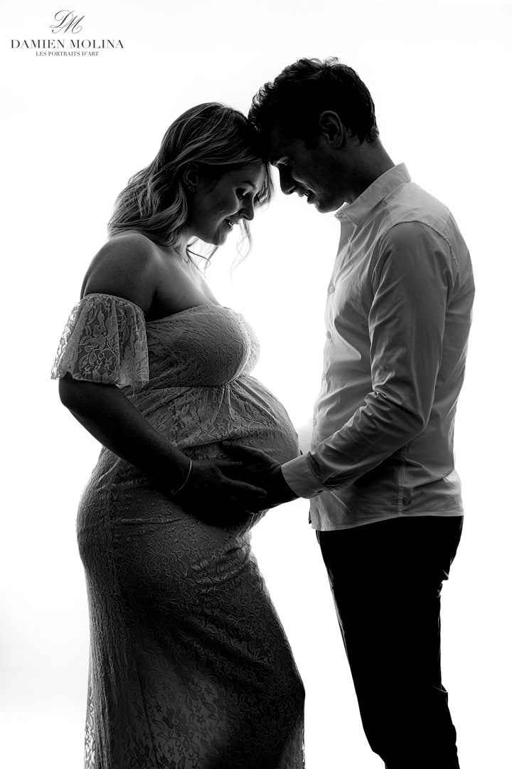 Portrait de grossesse complice et lumineux à Strasbourg (67) - Damien Molina - Photographe Portrait en noir et blanc d’un couple attendant un enfant, se tenant tête contre tête avec tendresse, leurs mains posées sur le ventre de la future maman vêtue d’une robe en dentelle, réalisé par Damien Molina à Strasbourg (67).