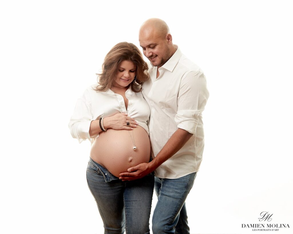 Photographe grossesse en Alsace : Complicité et élégance à Strasbourg - Damien Molina - Photographe Photo lumineuse d’un couple attendant un enfant, la future maman en chemise blanche et jean, avec le futur papa tenant délicatement son ventre, capturée par Damien Molina en Alsace.