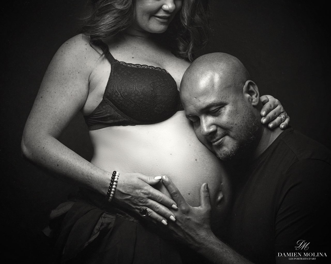 Portrait de grossesse intime en clair-obscur à Strasbourg - Damien Molina - Photographe Portrait en noir et blanc d'un couple attendant un enfant, le futur père écoutant le ventre de sa compagne enceinte, dans un style clair-obscur, réalisé par Damien Molina à Strasbourg.