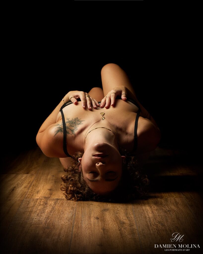 Portrait charme en pose renversée et clair-obscur en Alsace - Damien Molina - Photographe Portrait artistique d’une femme allongée sur le dos, mains sur son soutien-gorge, capturé en clair-obscur lors d’une séance photo charme en Alsace.