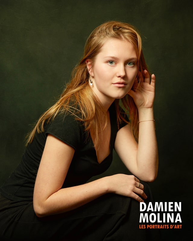 Signer les photos 3 - Damien Molina - Photographe Portrait of a young woman with blond hair in a black dress, posed against a dark studio backdrop with a calm expression.